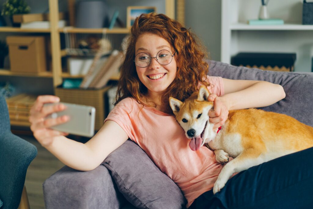 Beautiful girl taking selfie with puppy sitting on sofa at home using Zepeel to create a video profile on dating app