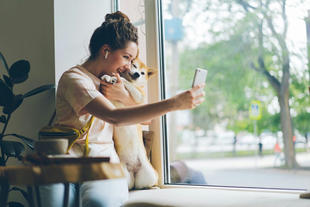 Cheerful lady taking selfie with doggy in cafe using Zepeel dating app