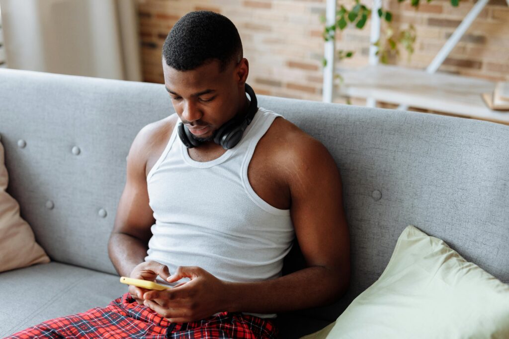 Man in white tank top sitting on couch using using Zepeel video date app and sending an ice breaker message